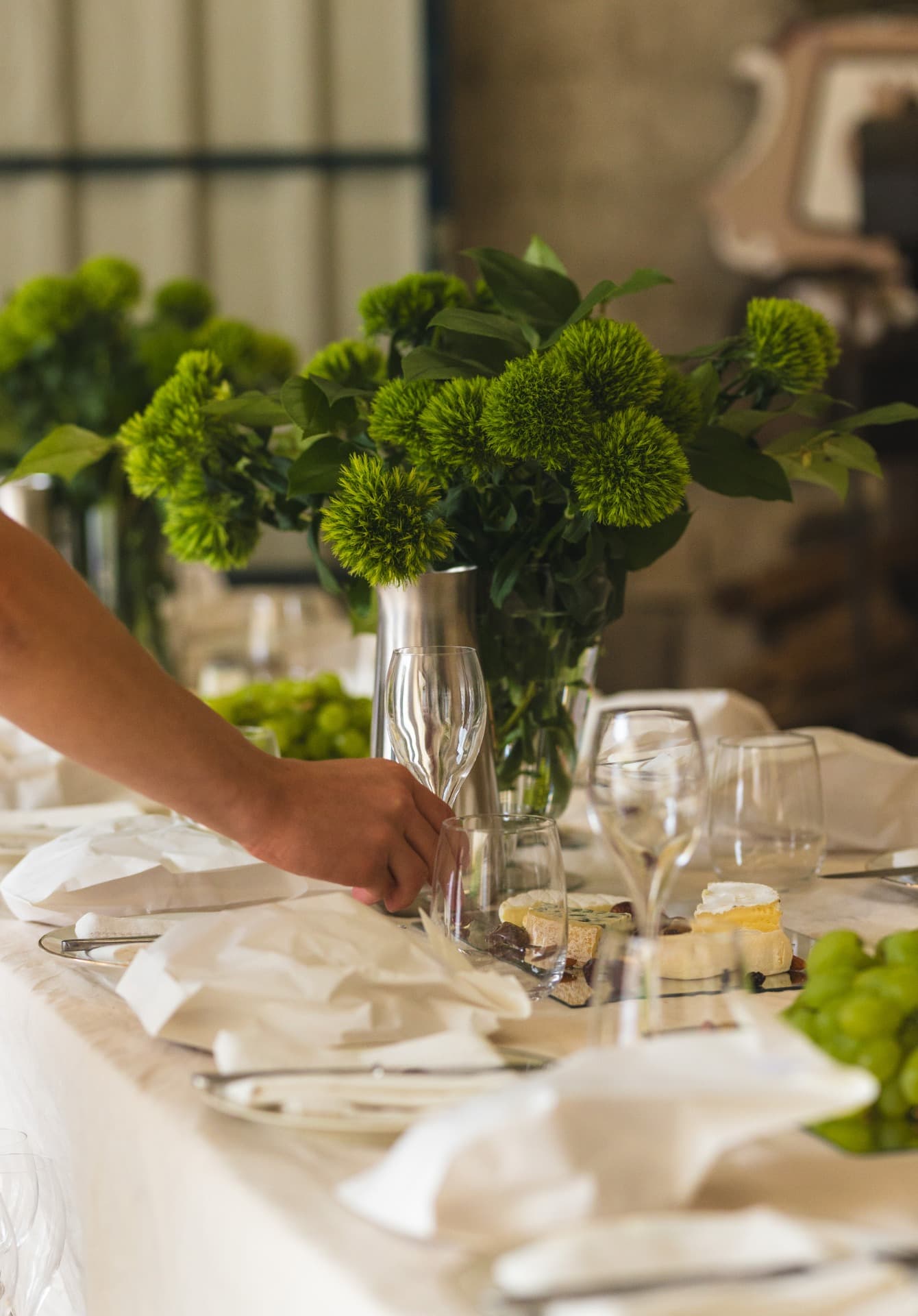 Ein Tisch wird mit Weingläsern und grünen Blumengestecken gedeckt.
