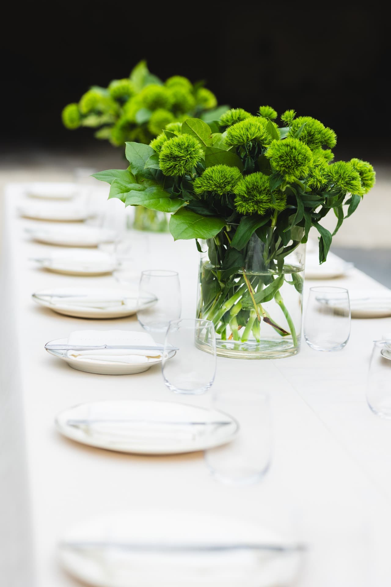 Lange tafel van HOUSEWINE À TABLE, gedekt met witte borden, glazen en groene bloemstukken.